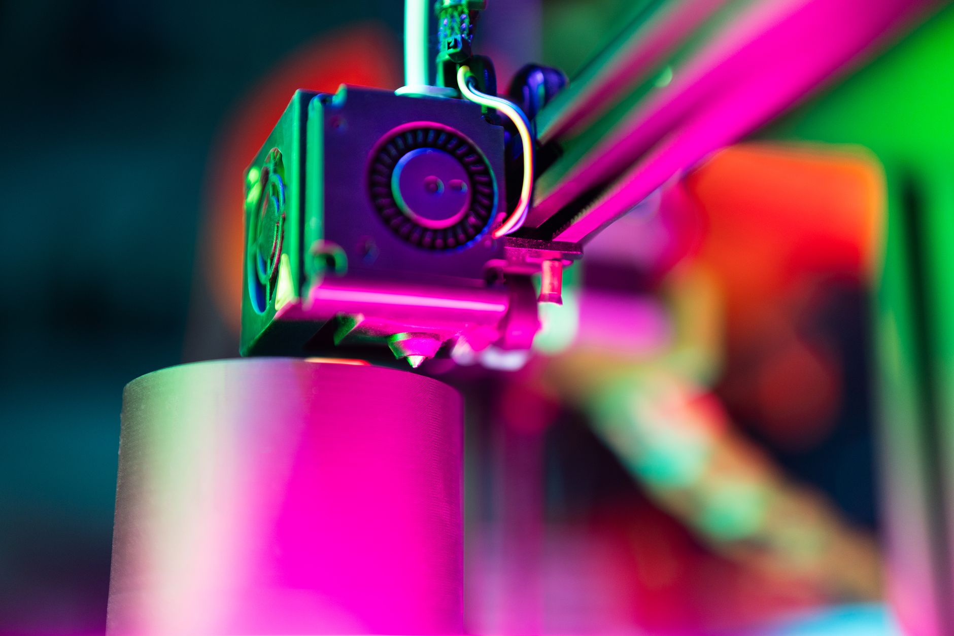 Detalhe do bico e extrusor de impressora 3D sob iluminação, mostrando o caminho do filamento