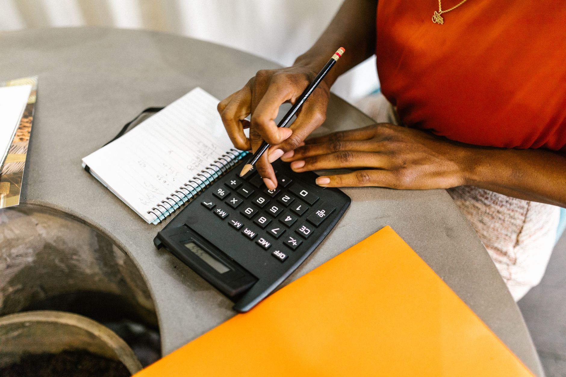 Pessoa fazendo contas com calculadora e caderno, definindo a margem da peça